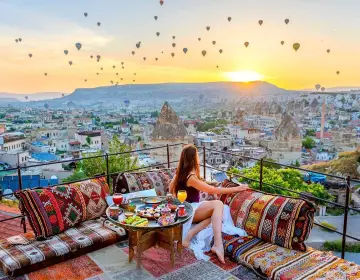 Woman on terrace watching sunrise and city balloons