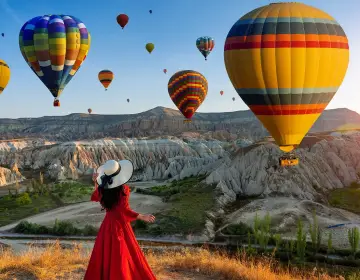 Woman in red dress posing with Cappadocia balloons