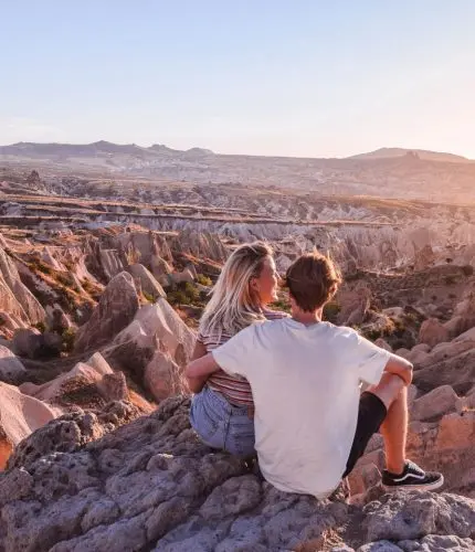 Couple on cliff edge at sunset overlooking valley