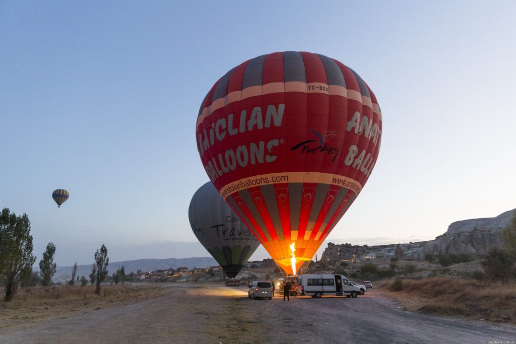 Hot air balloon being inflated with a burner flame before sunrise in Cappadocia, with Anatolian Balloons text visible.