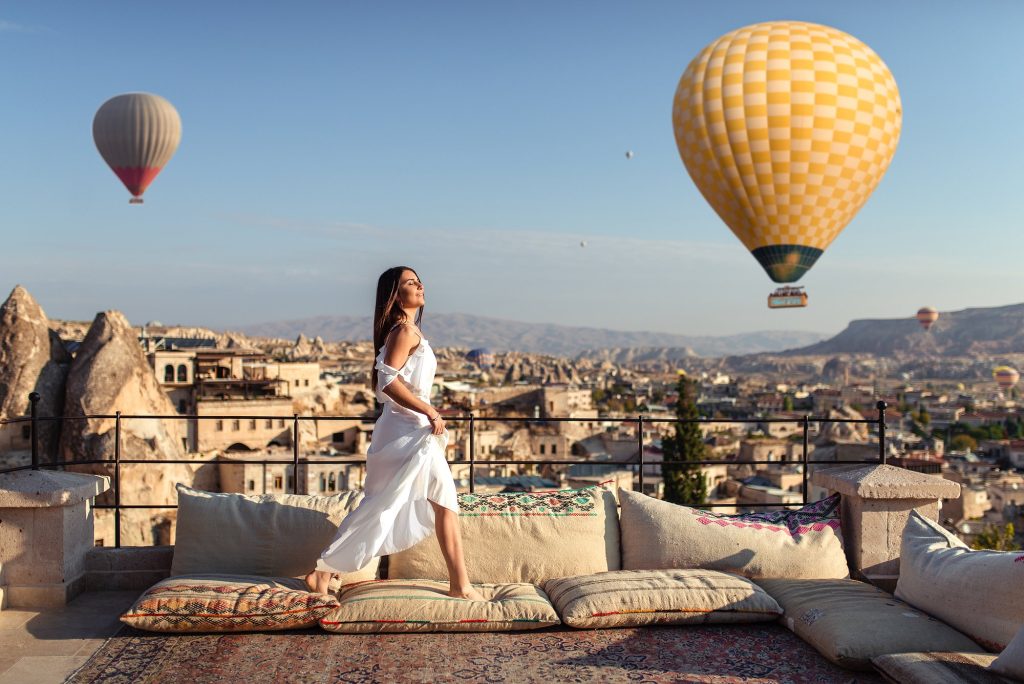Woman posing on terrace with hot air balloons sunrise