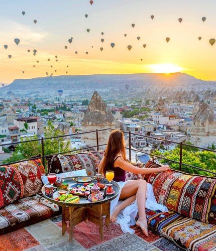 Woman on terrace watching sunrise and city balloons