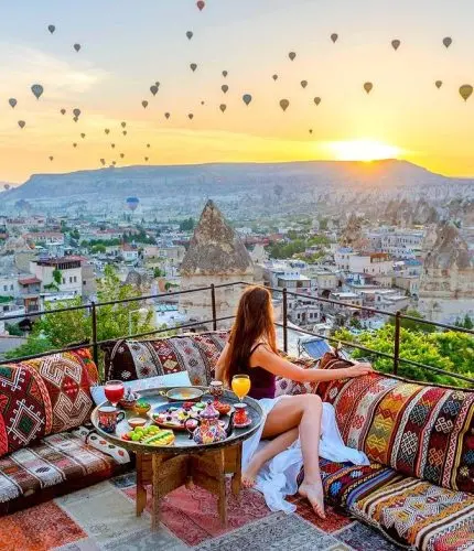 Woman on terrace watching sunrise and city balloons